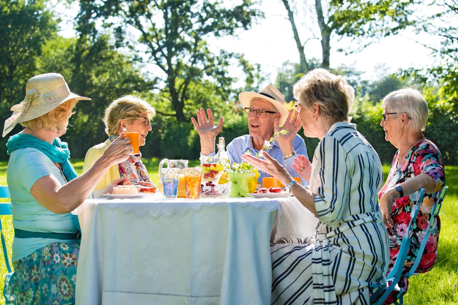 Senior friends having picnick with coffee and cake outdoors in sunshine.