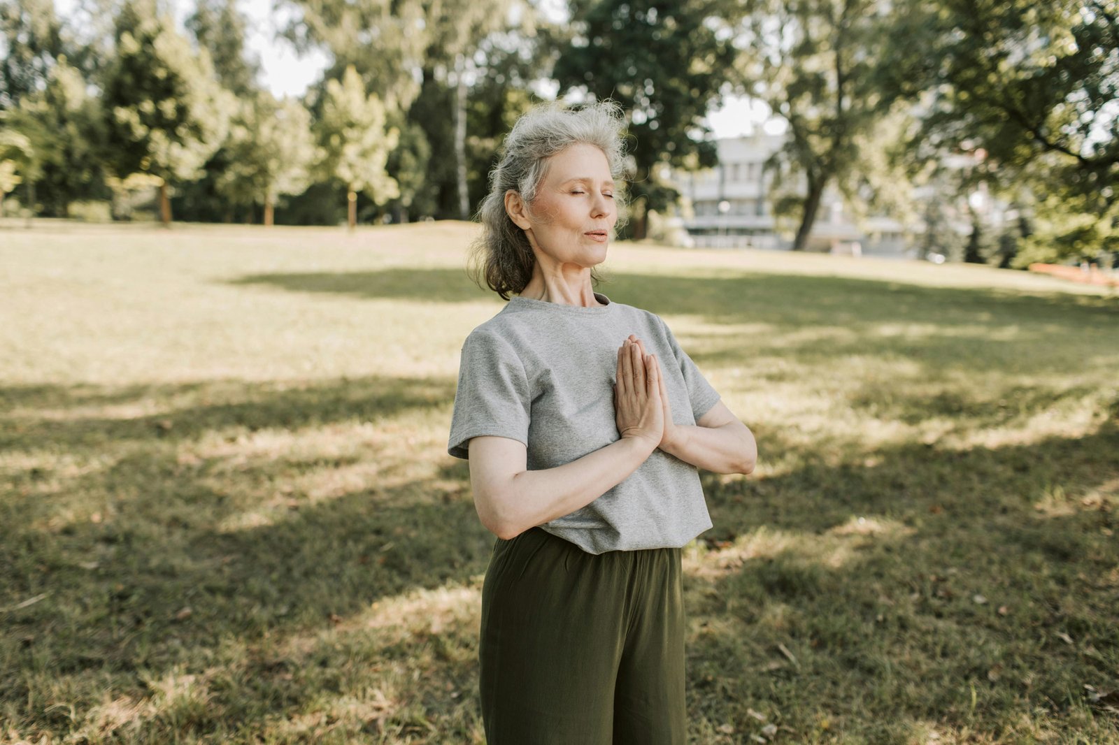 Woman with grey hair meditating outside in a sunny field